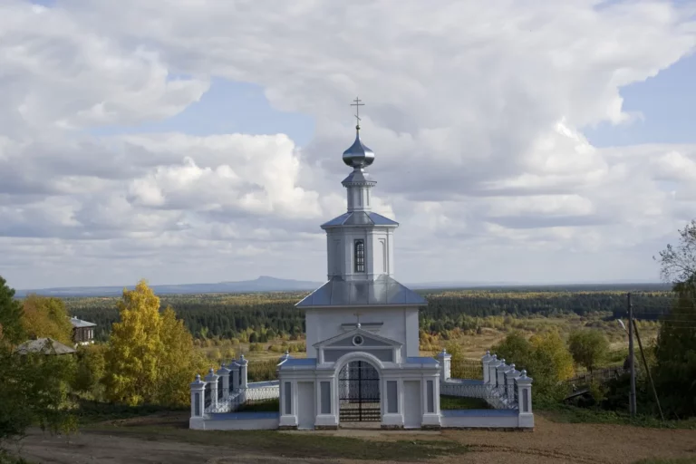 Белая часовня на холме под облачным небом